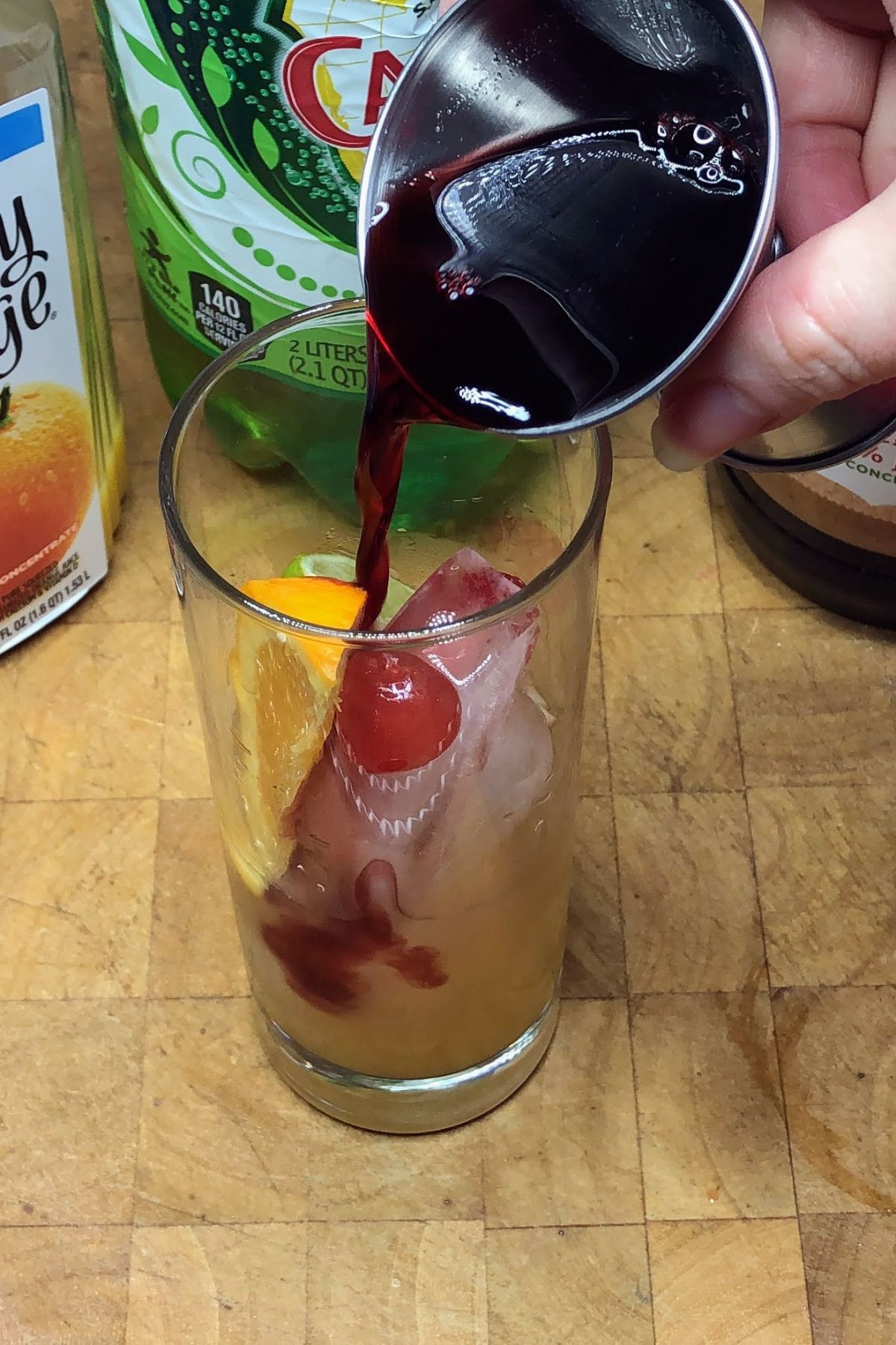 Pouring cherry juice from a jigger into a highball glass.