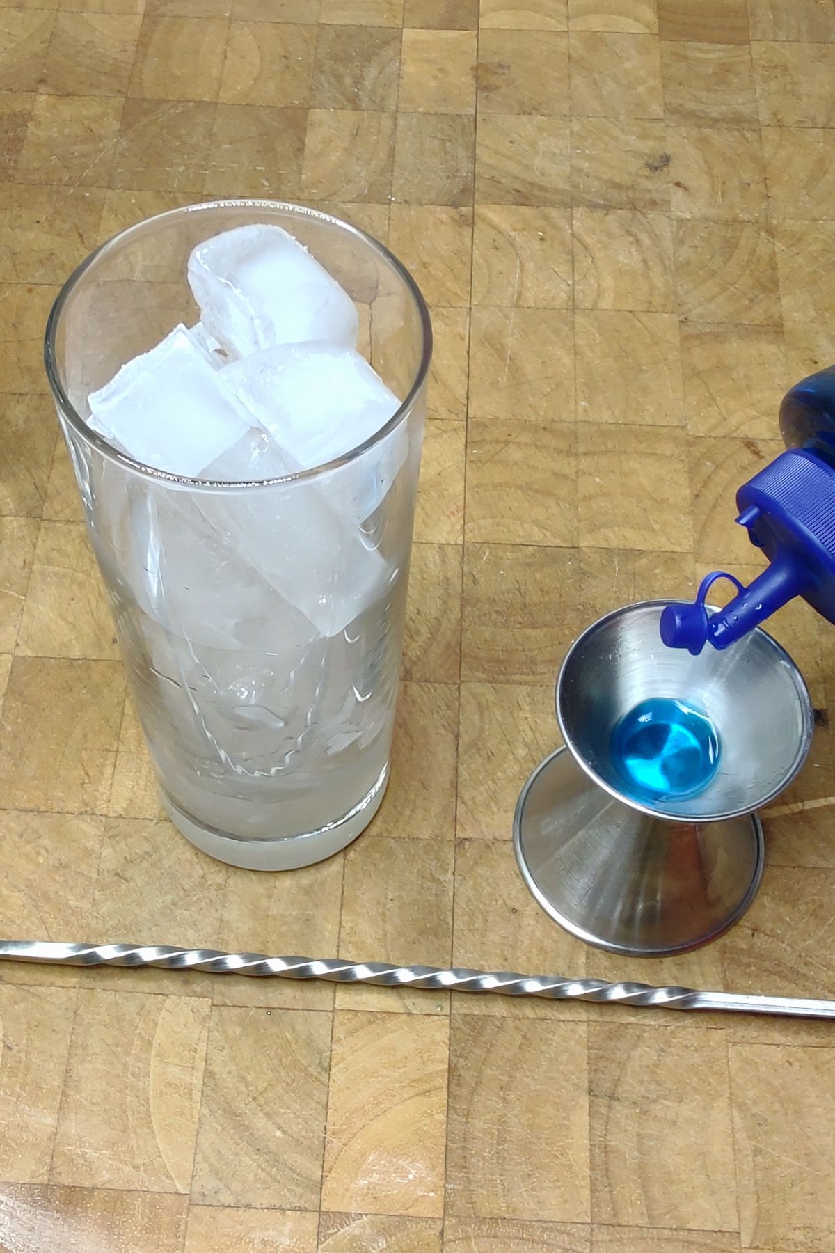 Pouring blue curacao into a jigger.