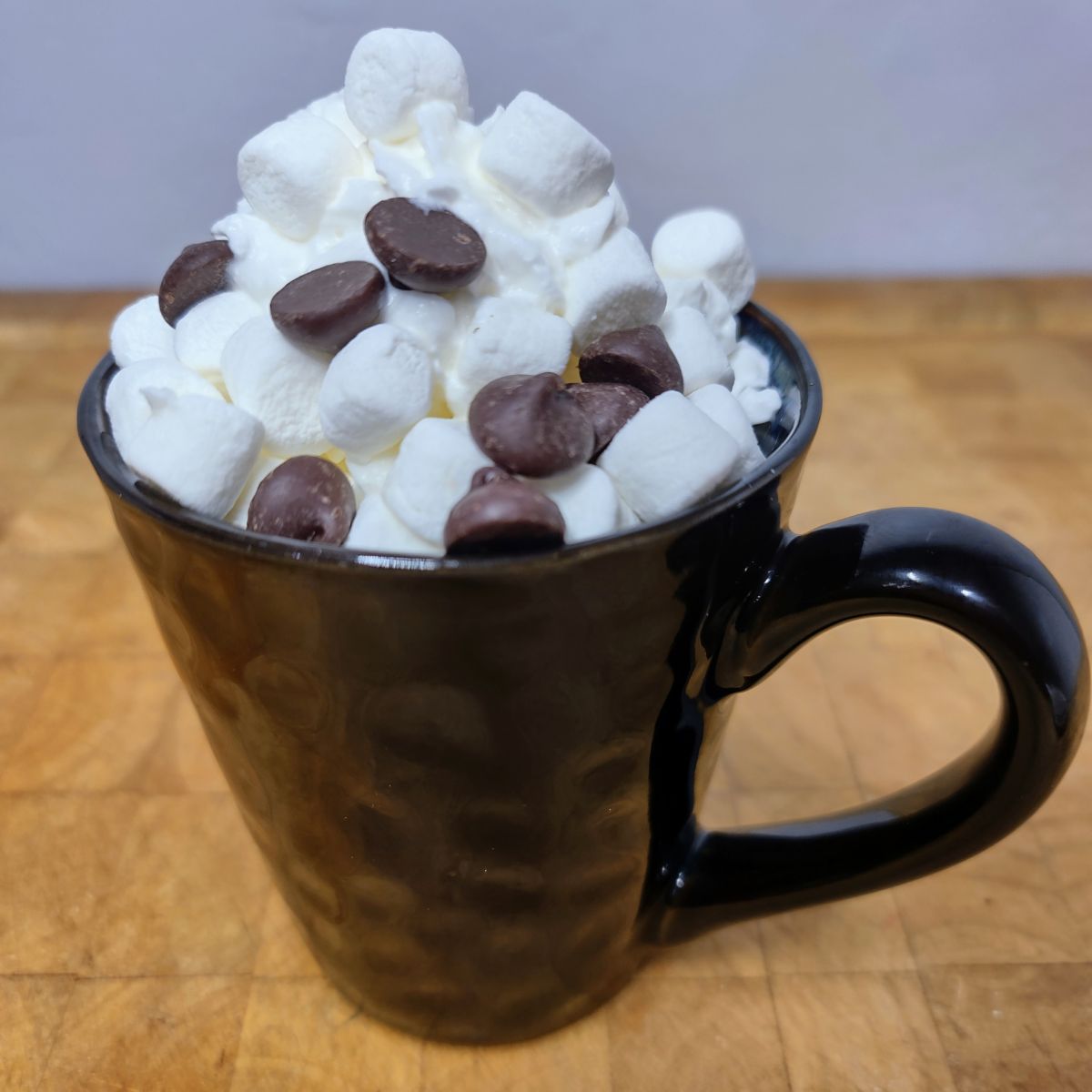 Orange hot chocolate in a mug with whipped cream, mini marshmallows and mini chocolate chips on top.