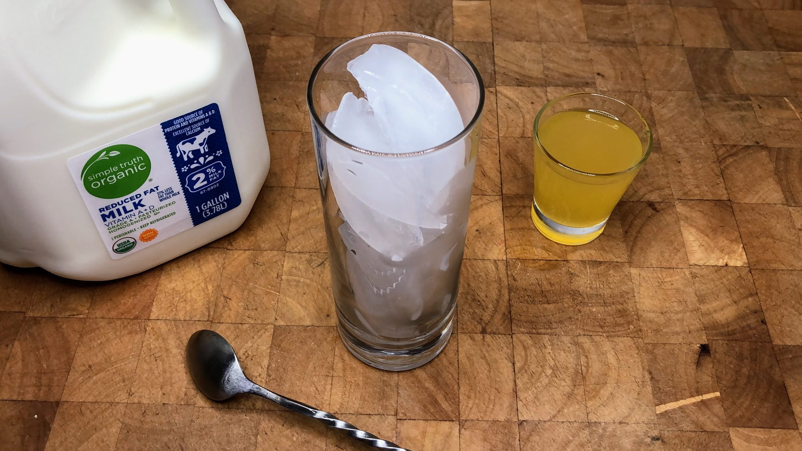 Milk and orange simple syrup next to a spoon and highball glass filled with ice.