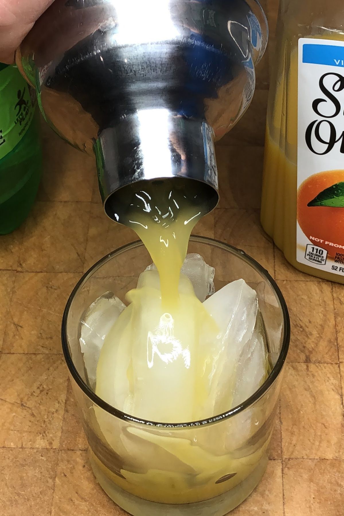 Pouring an orange mocktail from a shaker into a rocks glass.