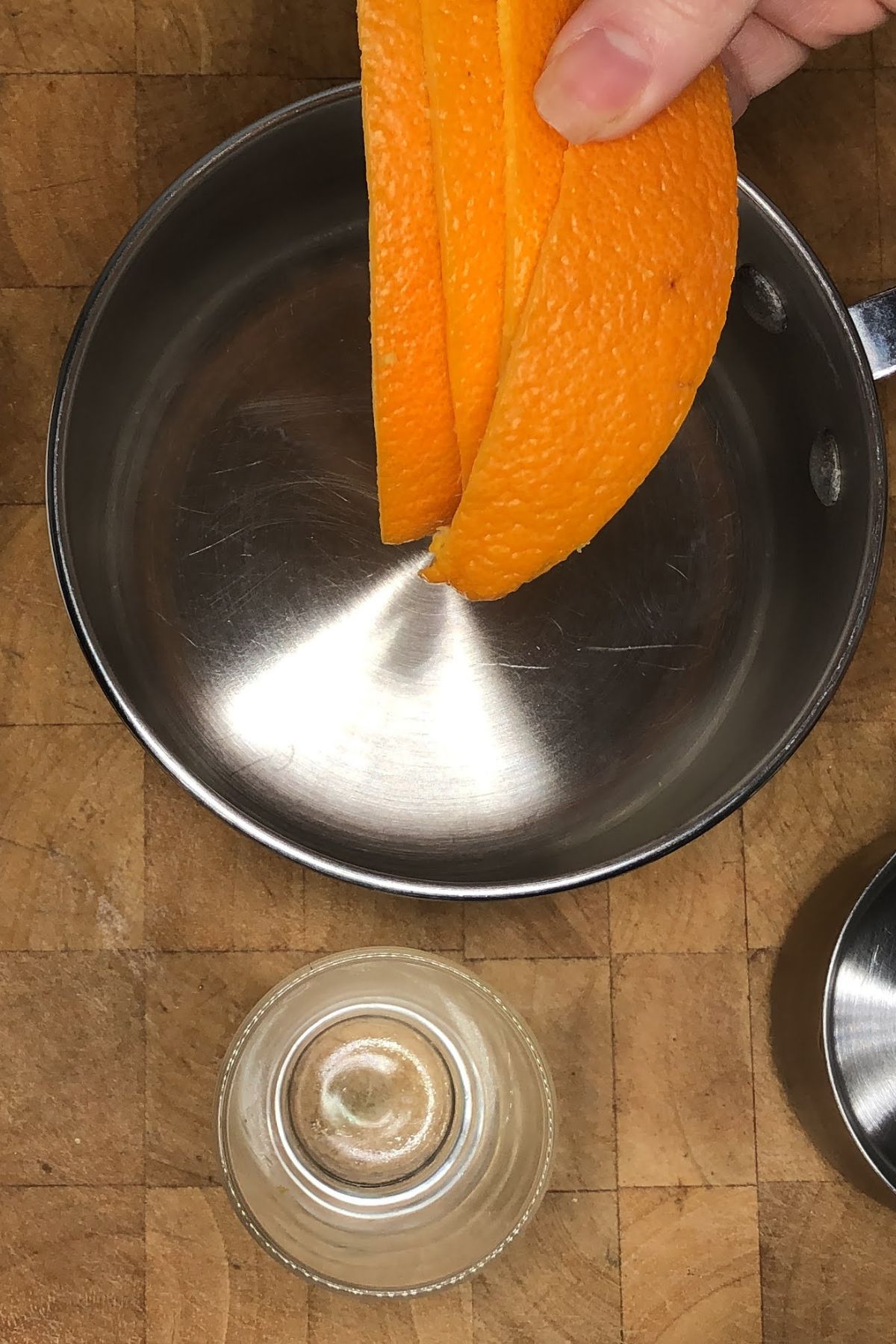 Adding three orange peels into a pot.