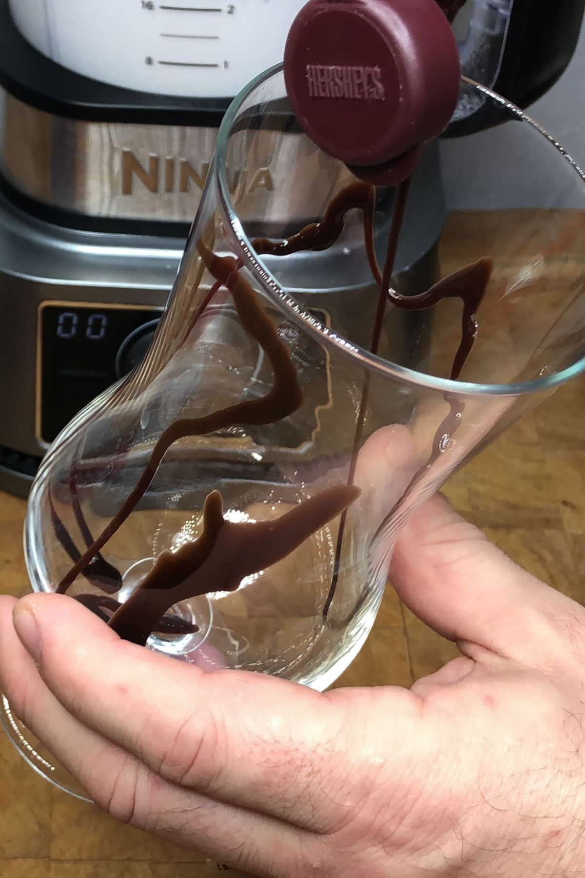 Drizzling chocolate syrup into a hurricane glass.