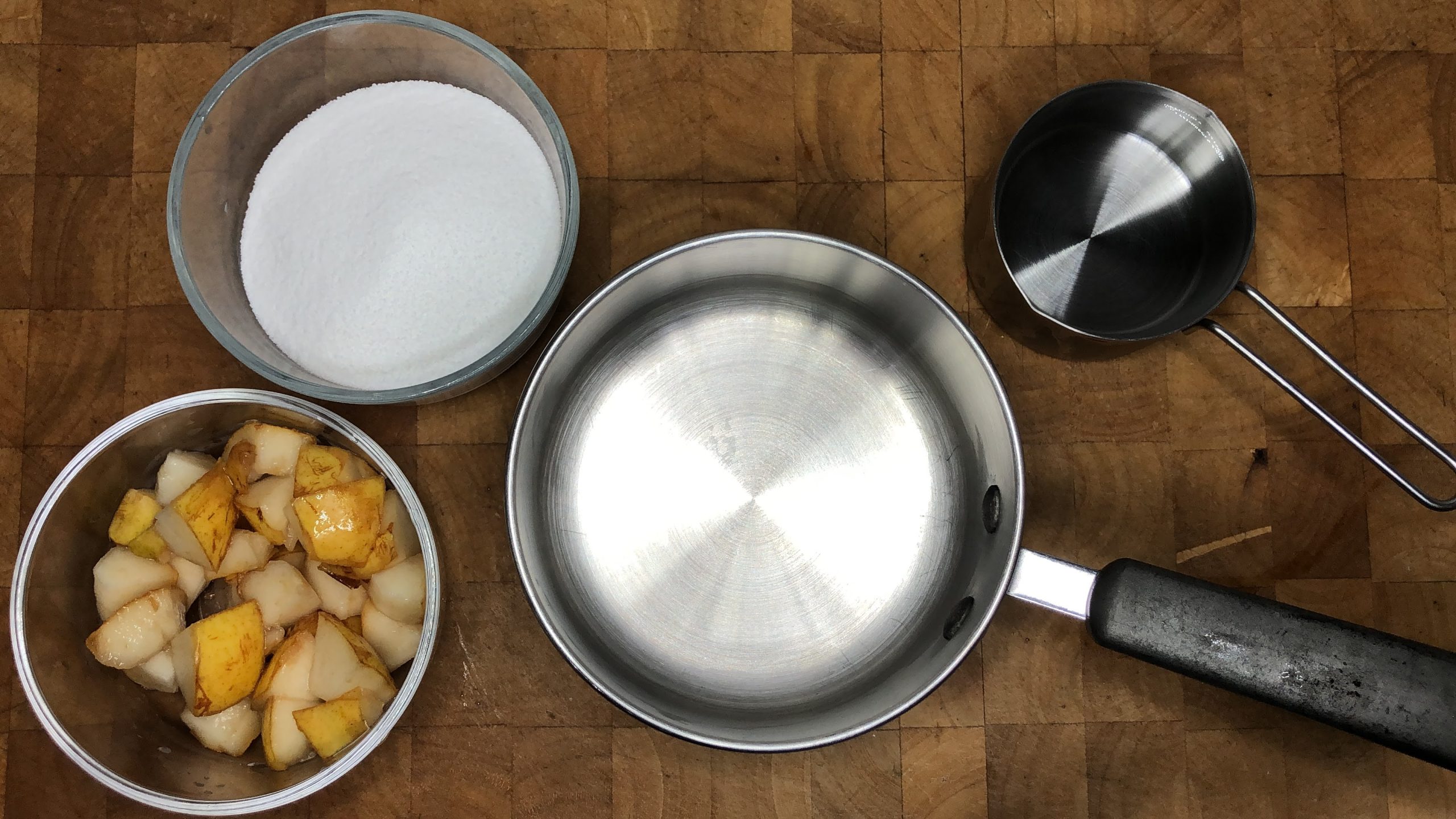 An empty pot next to bowls of sliced pears, sugar and water.