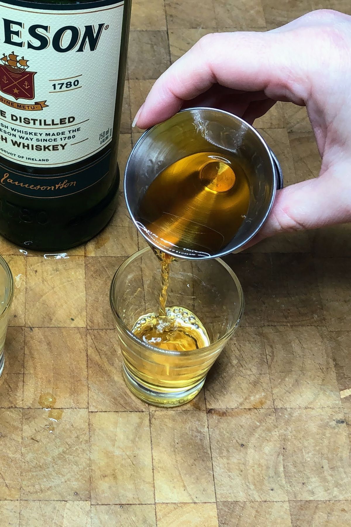 Pouring whiskey from jigger into shot glass.