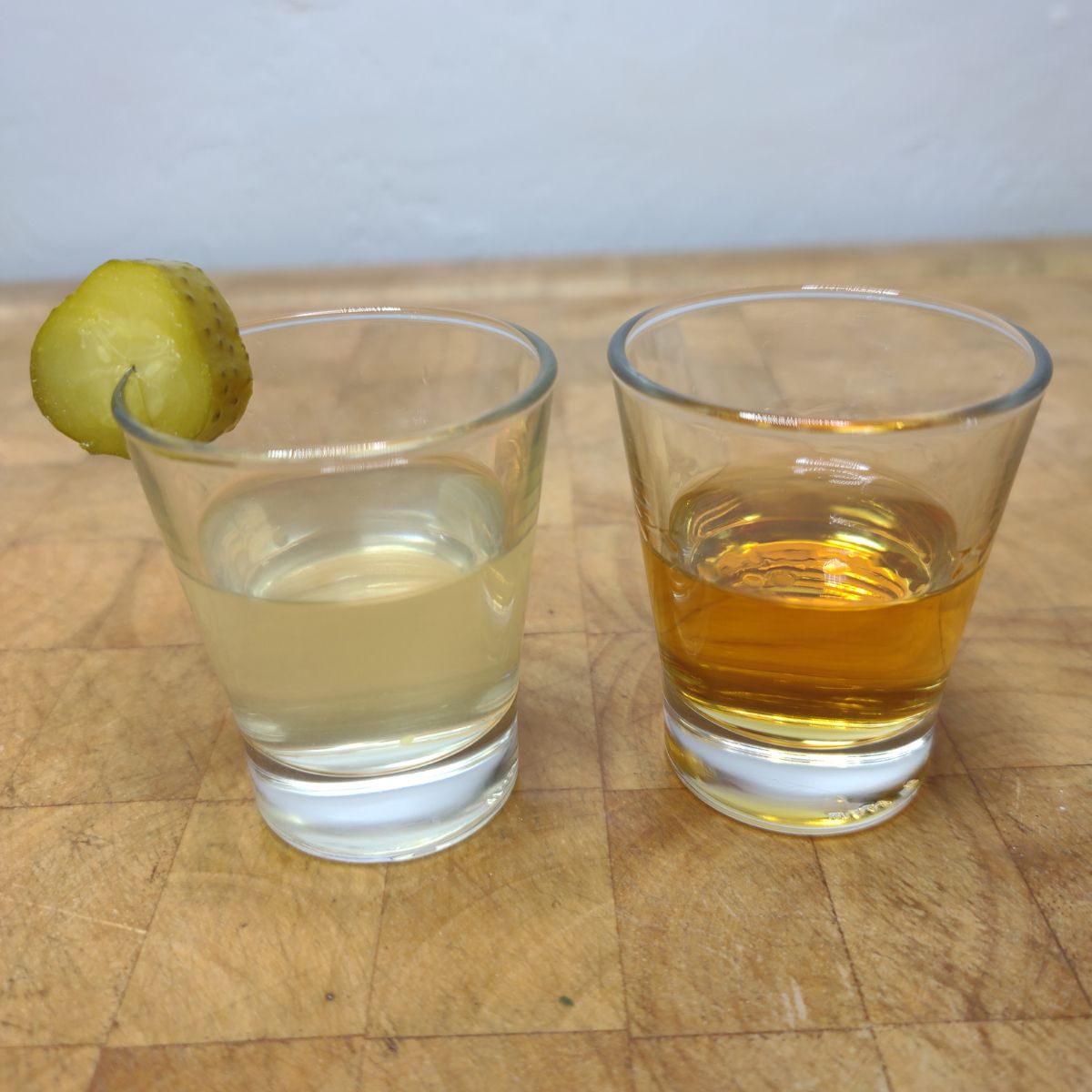 Pickleback shot with a pickle on the rim on a wooden table.