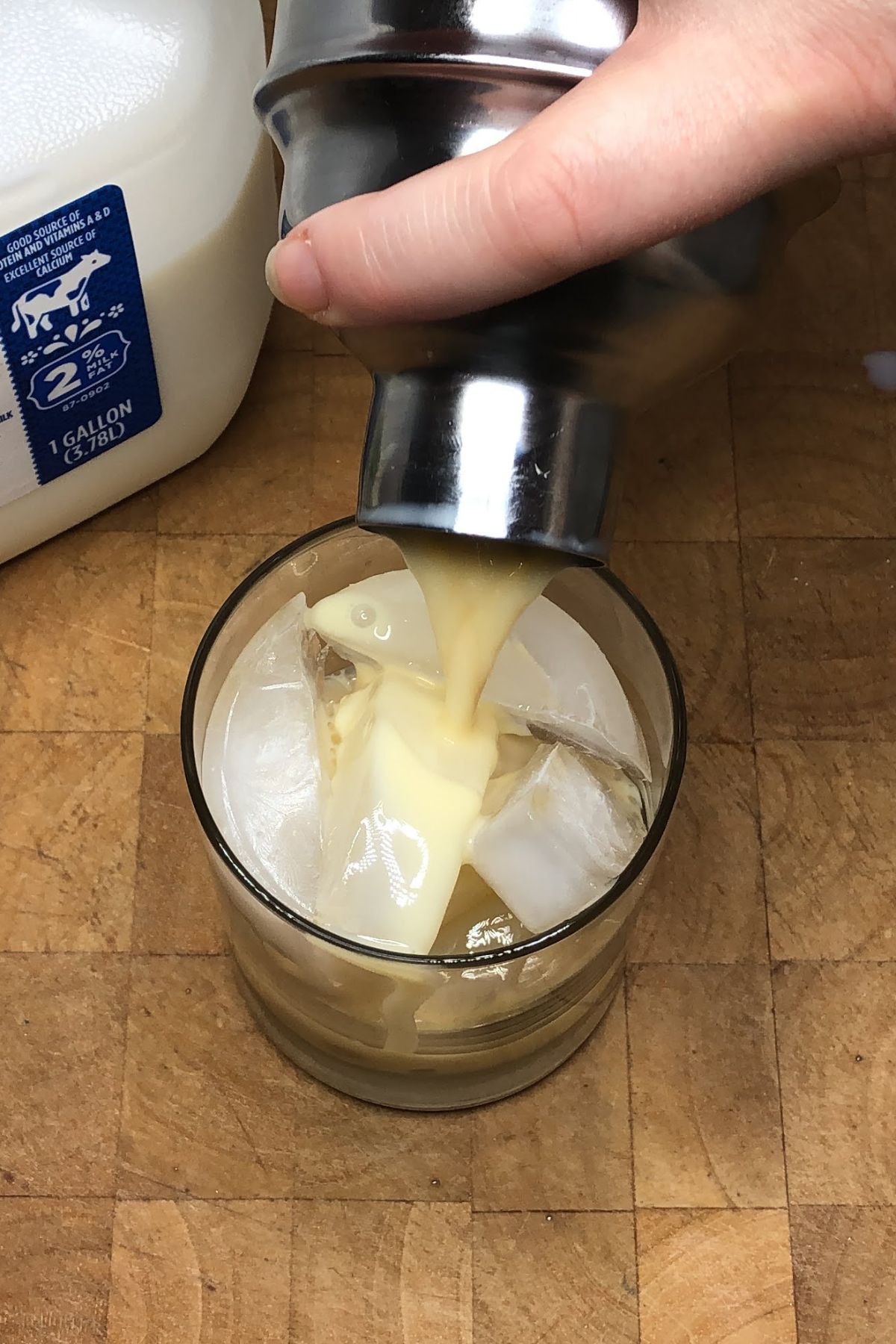 Pouring pumpkin milk from a shaker into a rocks glass.