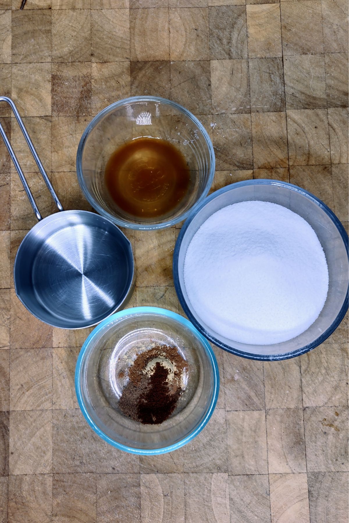 Bowls of water, sugar, pumpkin spice mix and vanilla extract on a wooden table.
