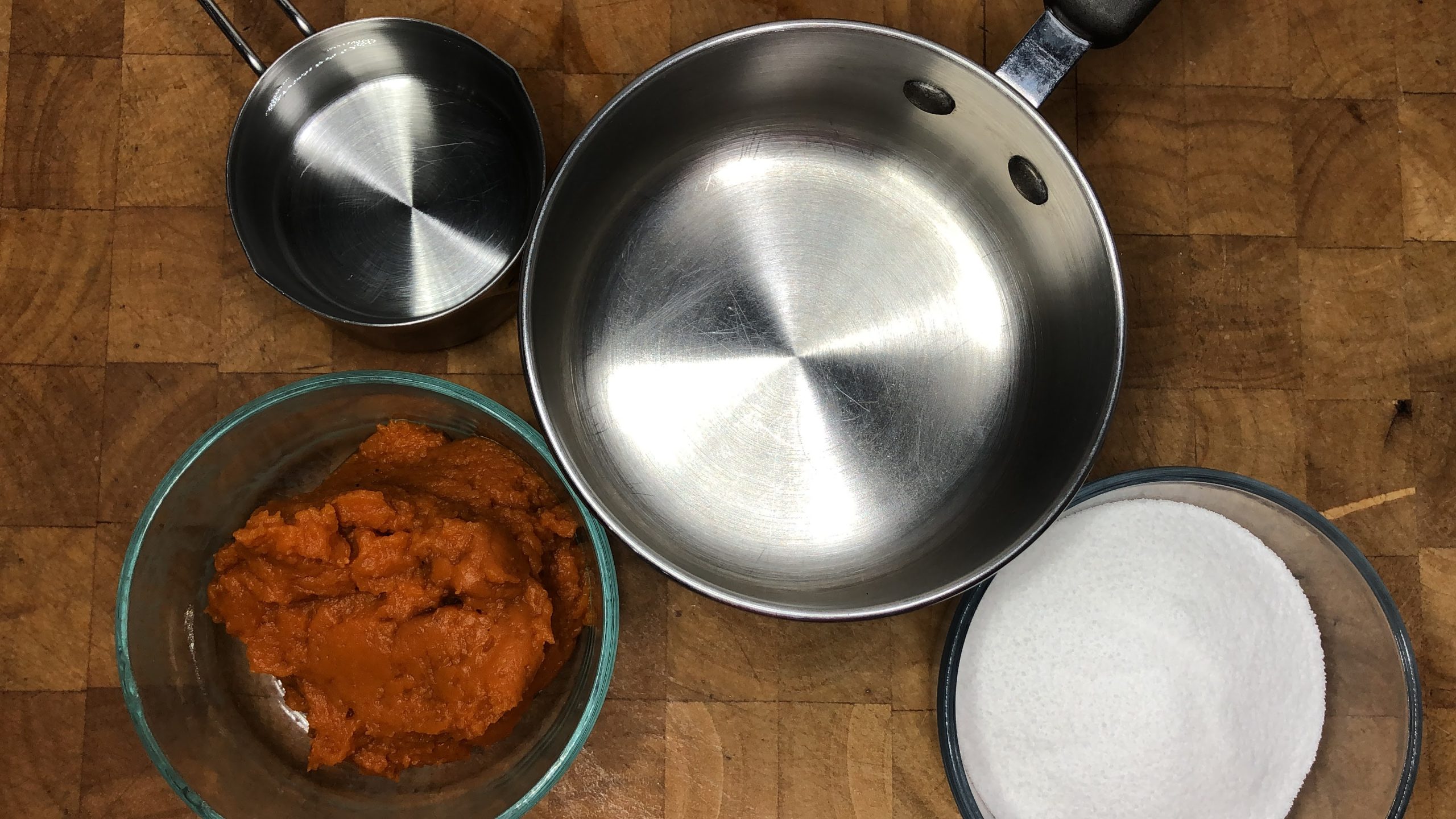 Bowls of pumpkin, sugar and water next to a saucepan.
