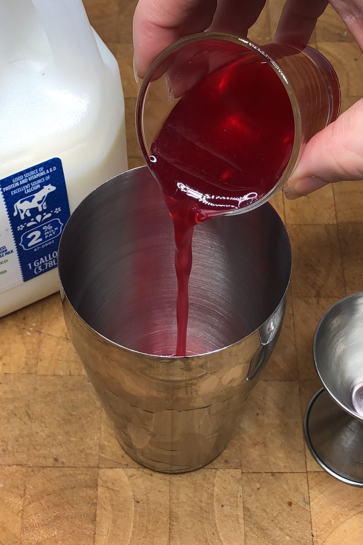 Pouring raspberry simple syrup into a cocktail shaker.