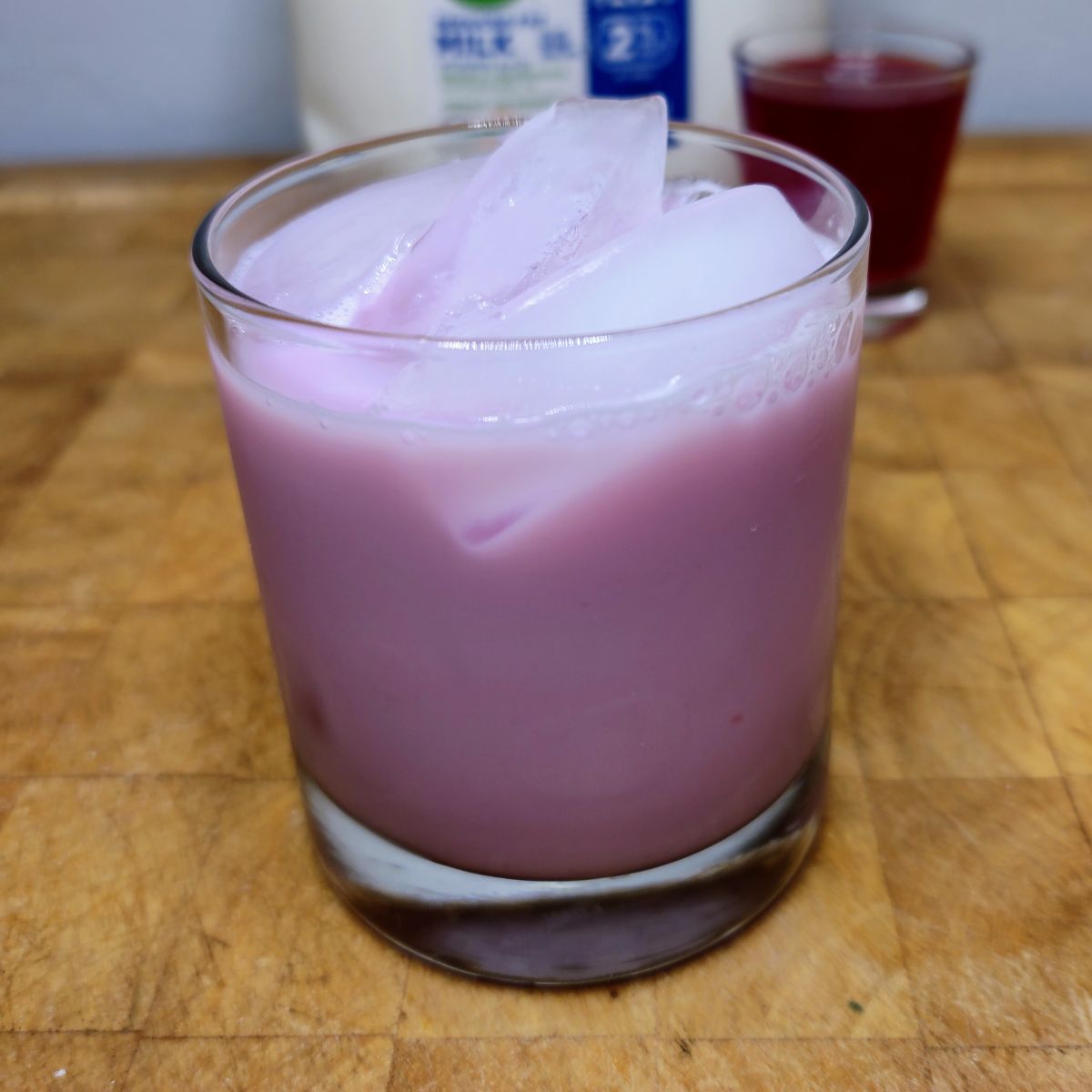 Raspberry milk in a glass on a wooden table with ingredients in the background.