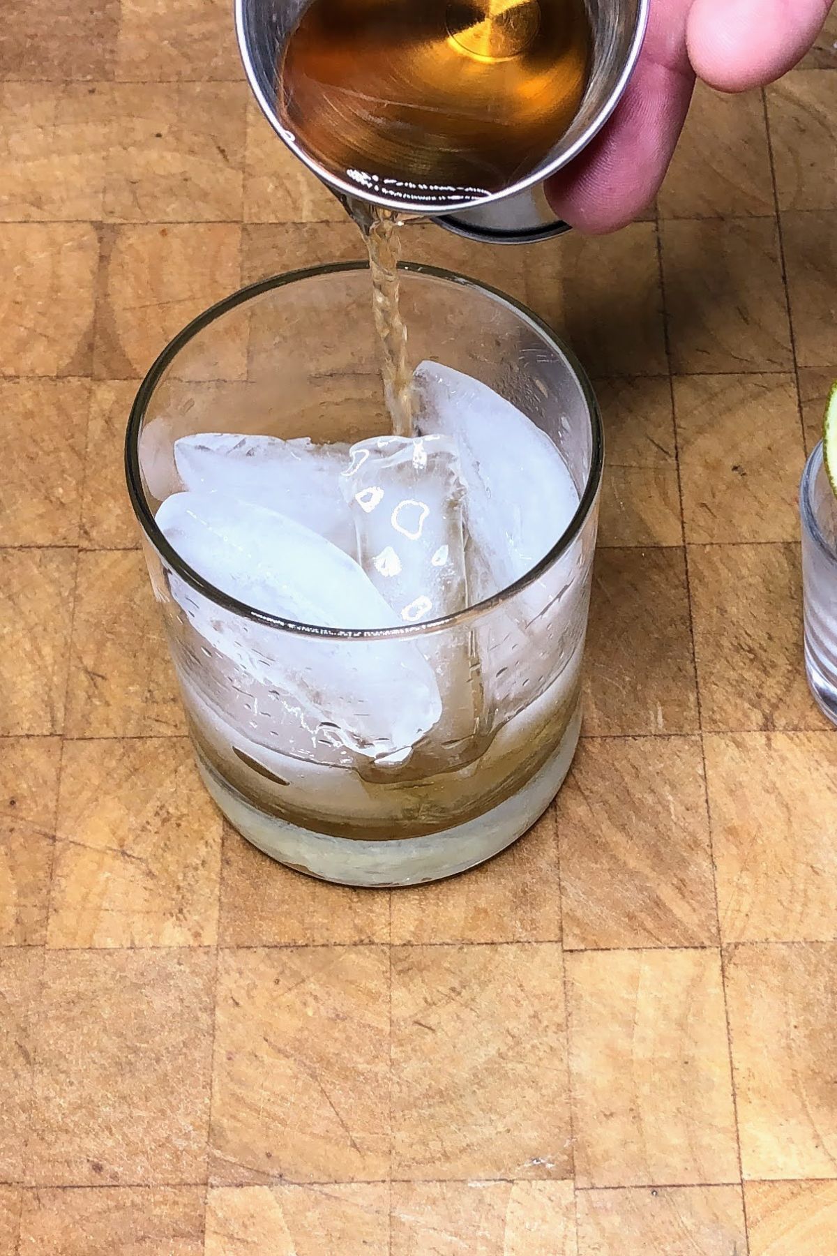 Pouring rum from a jigger into a rocks glass.
