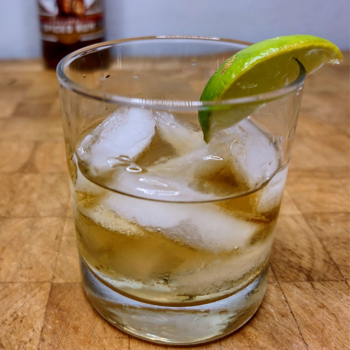 Rum on the rocks with a lime wedge on a wooden table.