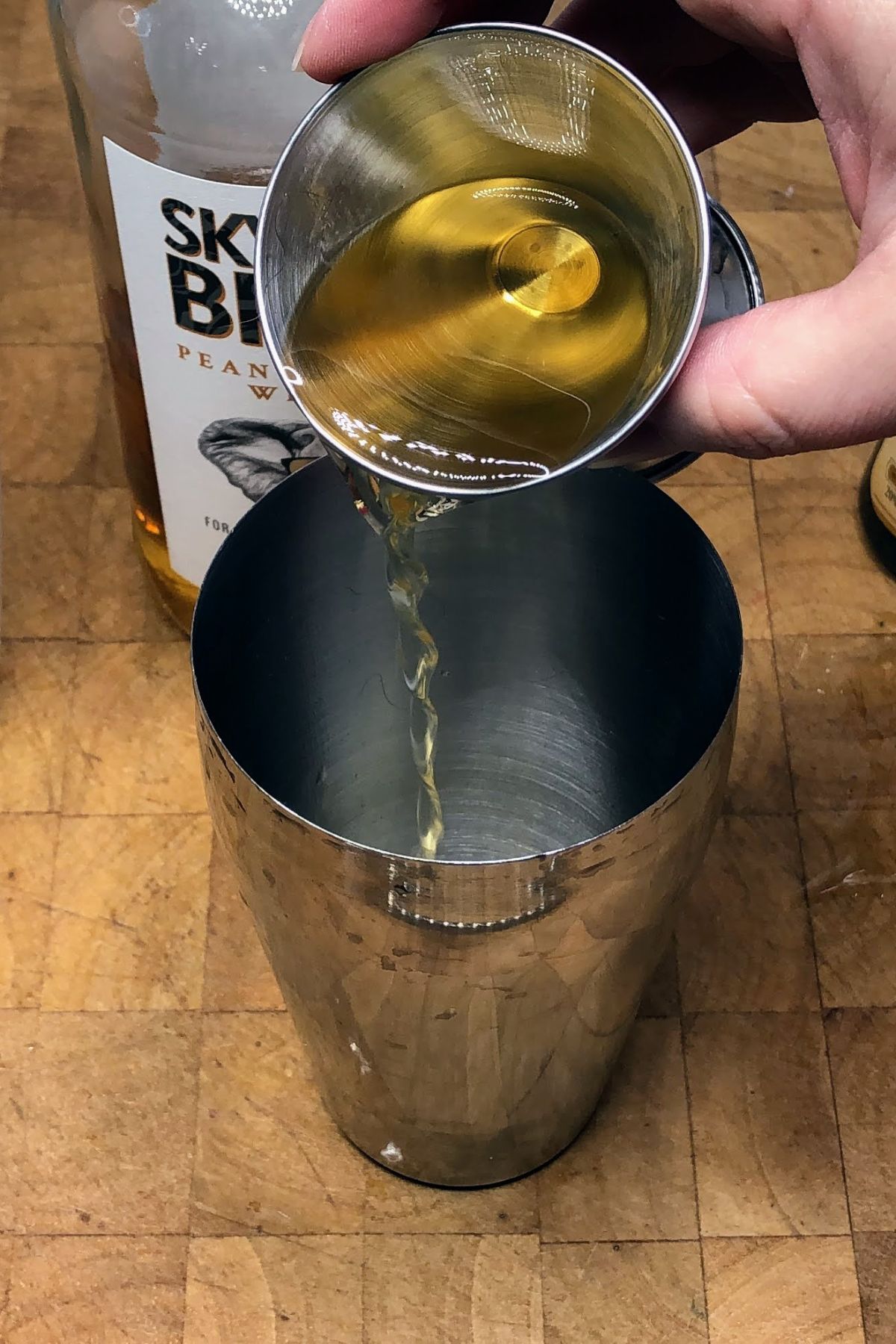 Pouring frangelico from a jigger into a shaker.