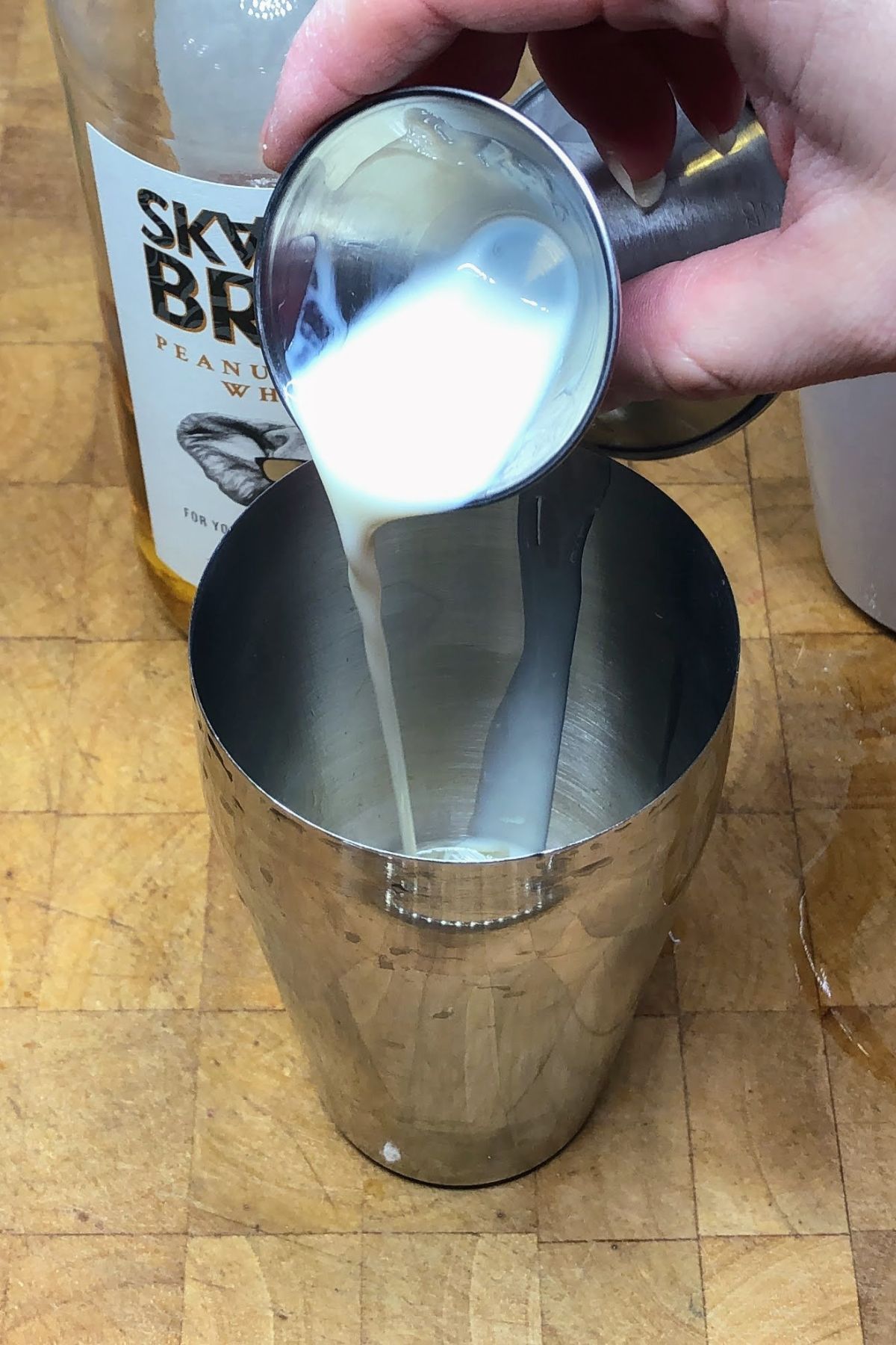 Pouring rumchata from a jigger into a shaker.