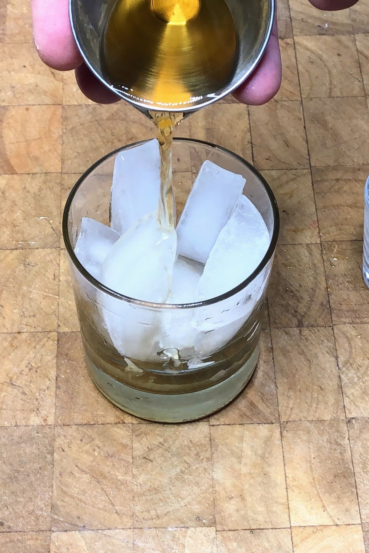 Pouring scotch from a jigger into a rocks glass.