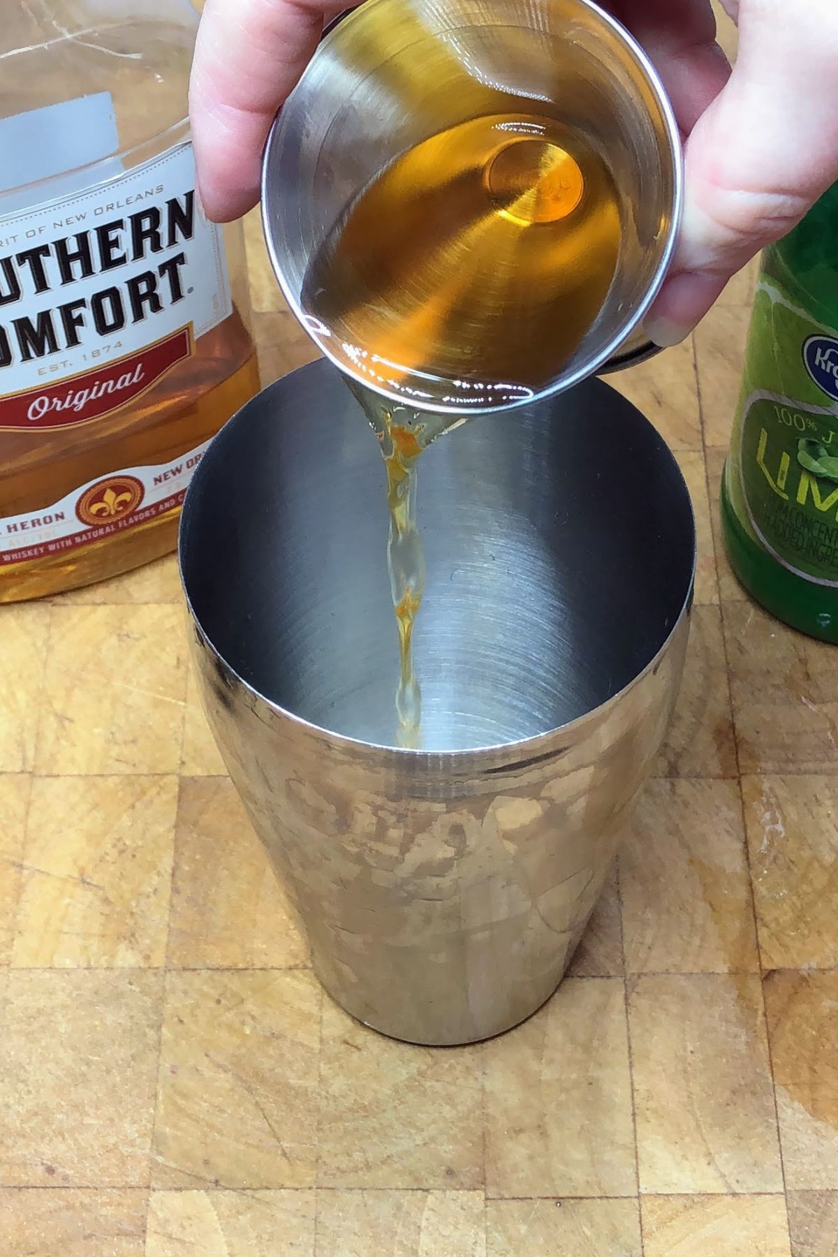Pouring southern comfort from a jigger into a shaker.