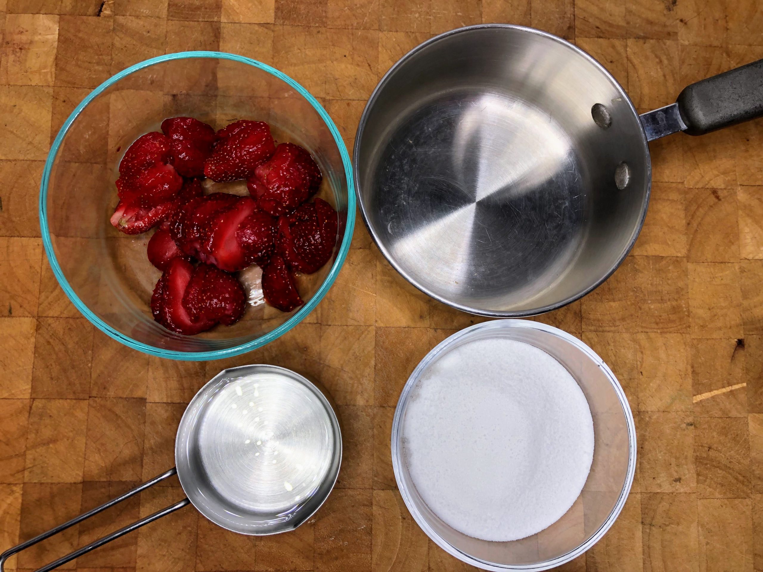 Bowl of strawberries, water and sugar next to a saucepan