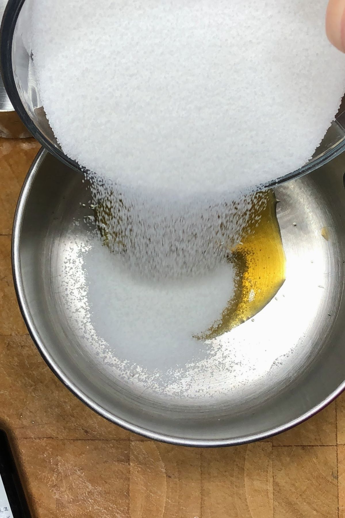 Pouring sugar into a saucepan with vanilla, butter and almond extract.