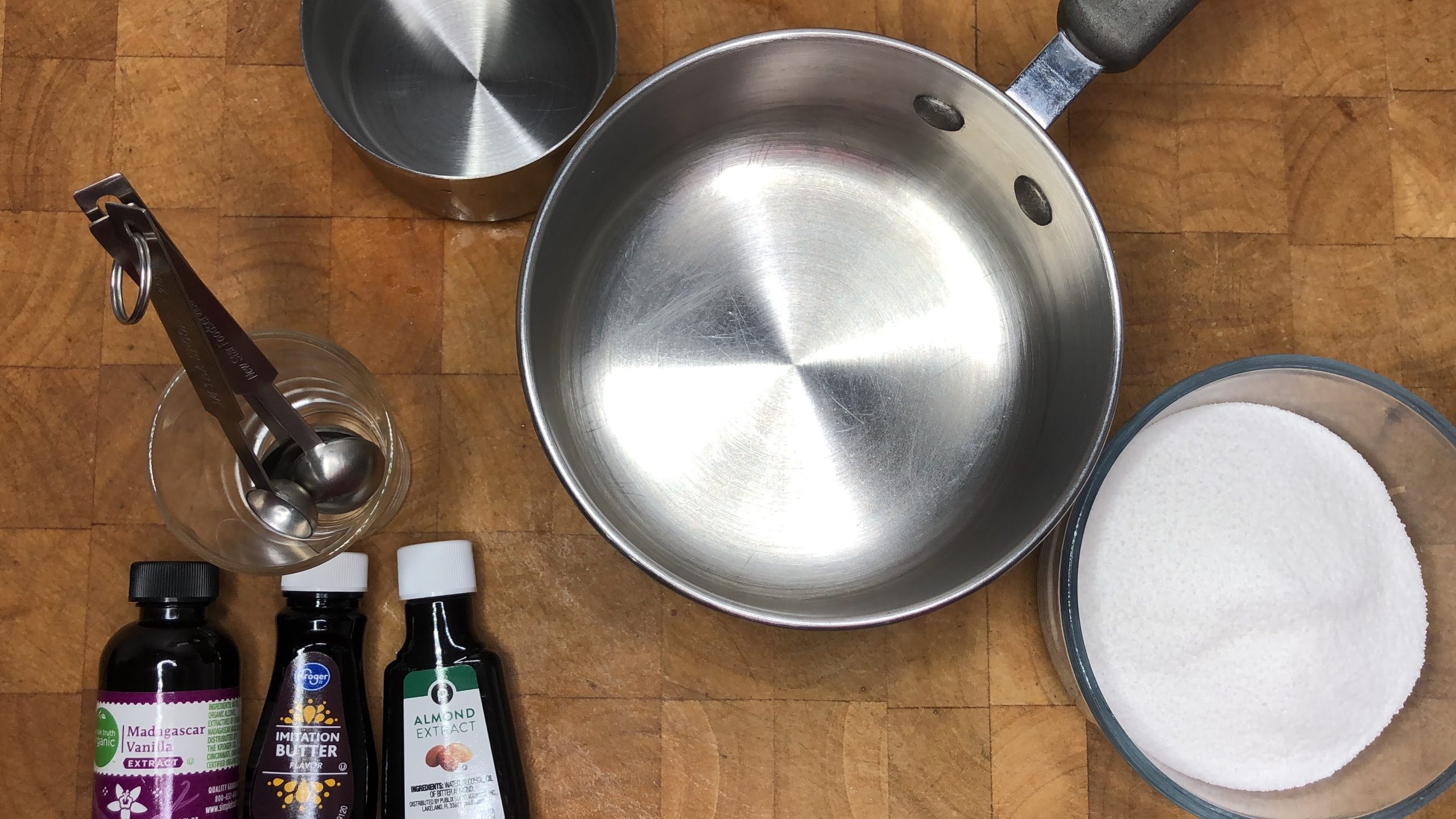 Bowls of sugar and water as well as vanilla, butter and almond extract next to a saucepan.
