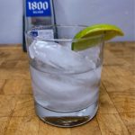 Tequila on the rocks with a lime wedge on a wooden table.