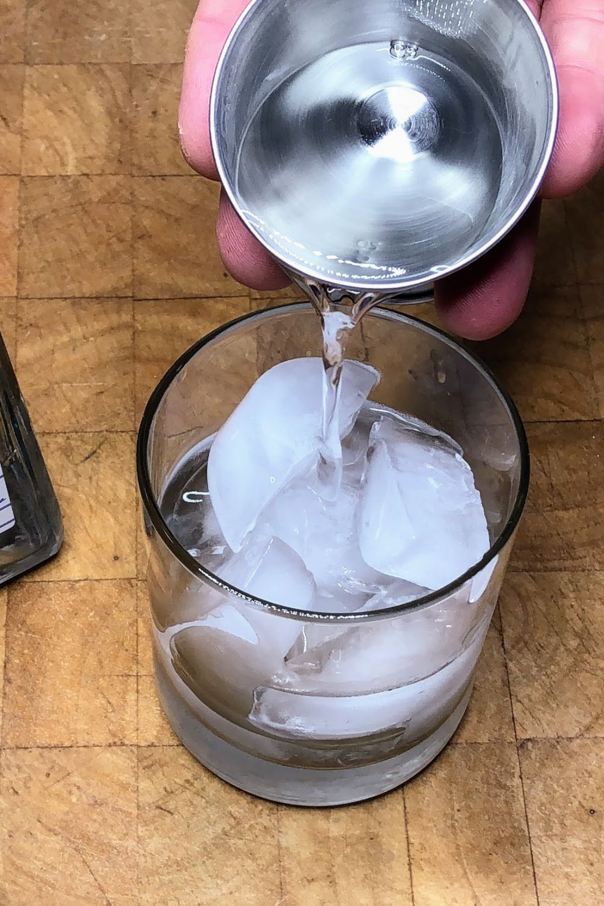 Pouring tequila from a jigger into a rocks glass.