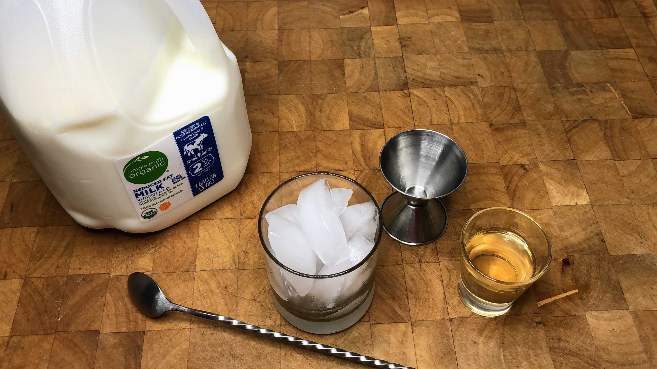 Vanilla simple syrup and milk next to a bar spoon, jigger and rocks glass filled with ice.