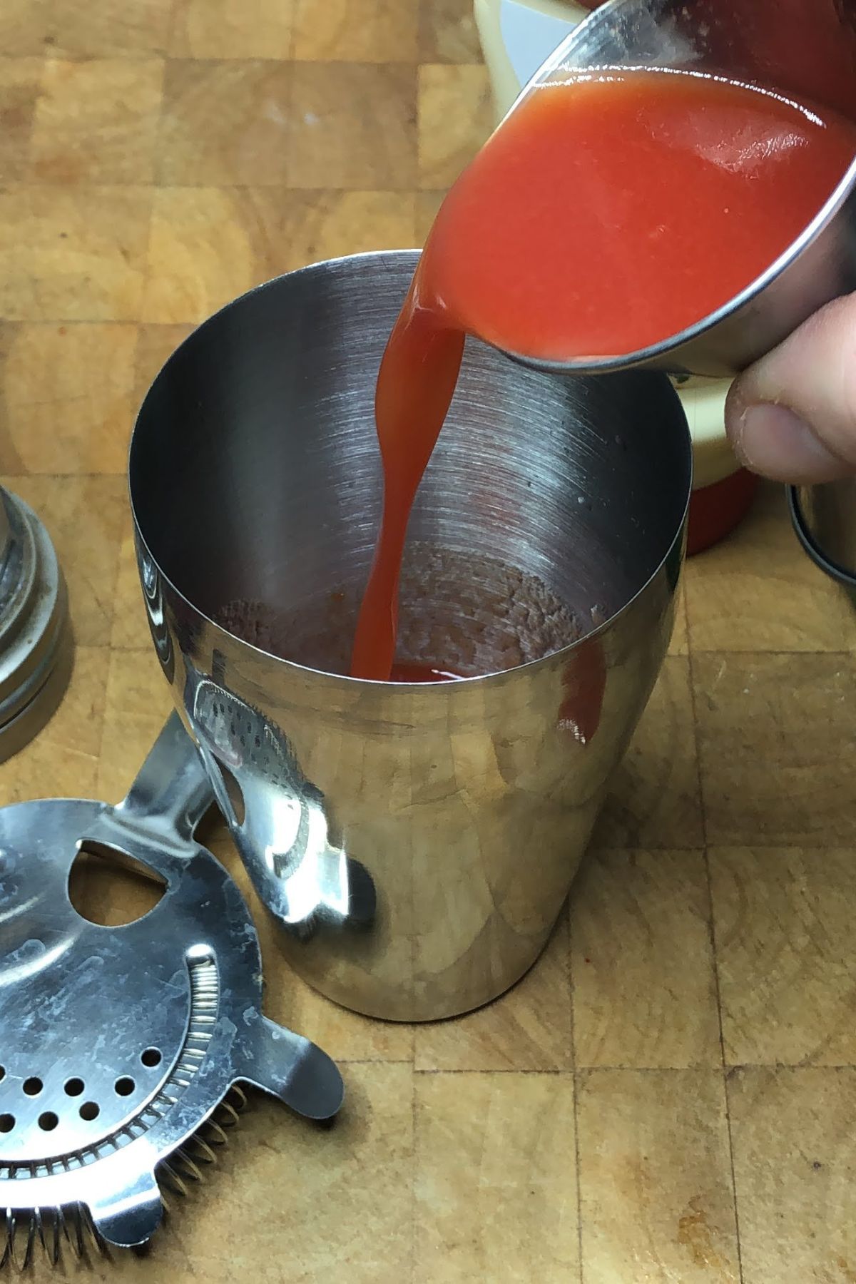 Pouring tomato juice from a jigger into a shaker.