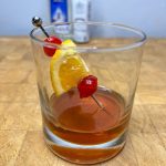 Virgin old fashioned with cherries and chunk of orange in the glass on a wooden table.