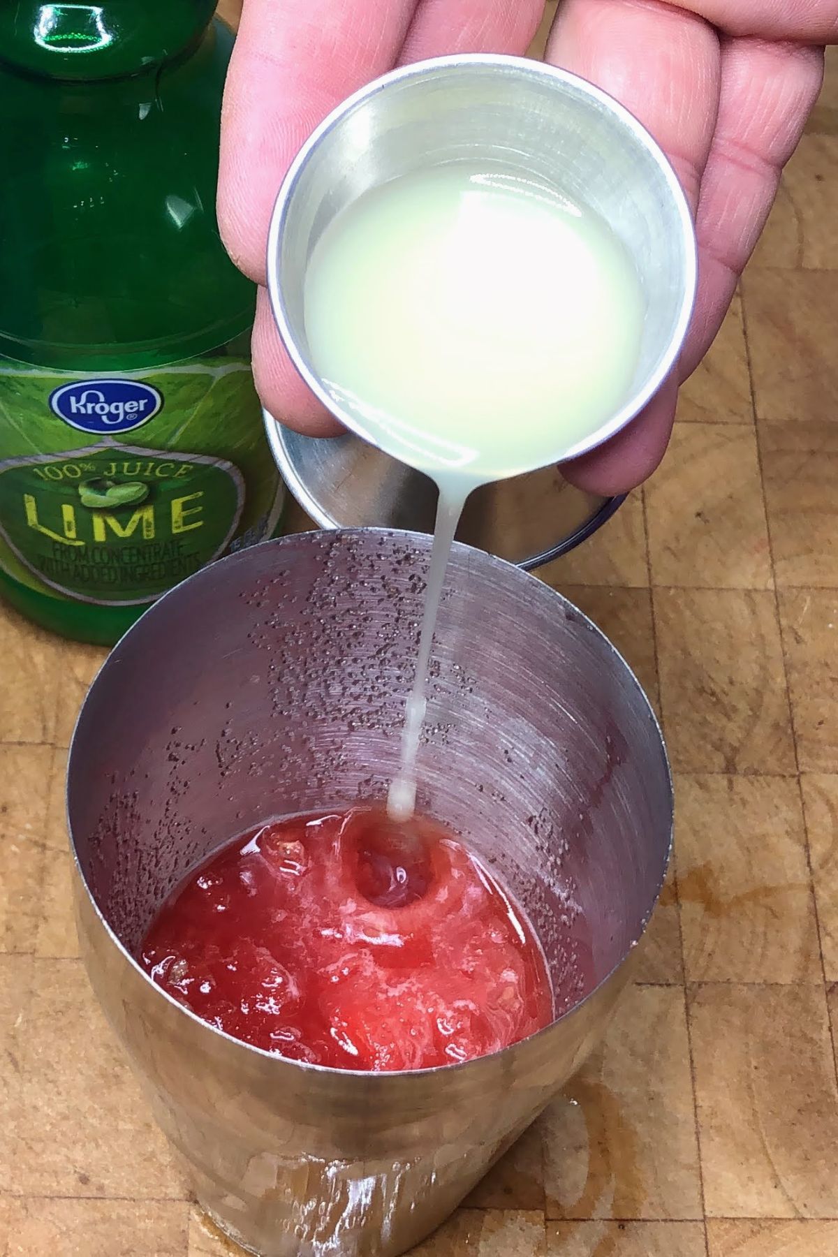Pouring lime juice from a jigger into a shaker.
