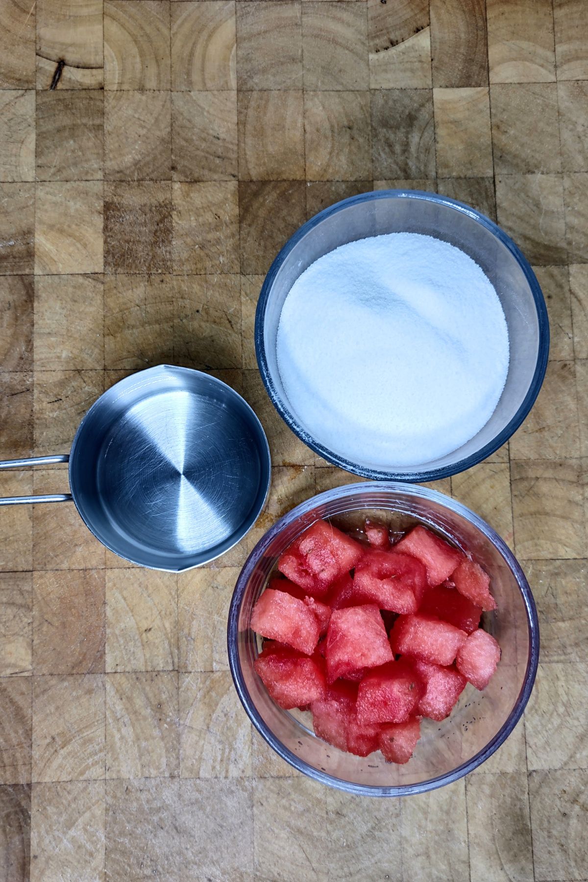 Bowls of sugar, water and diced watermelon on wooden table.