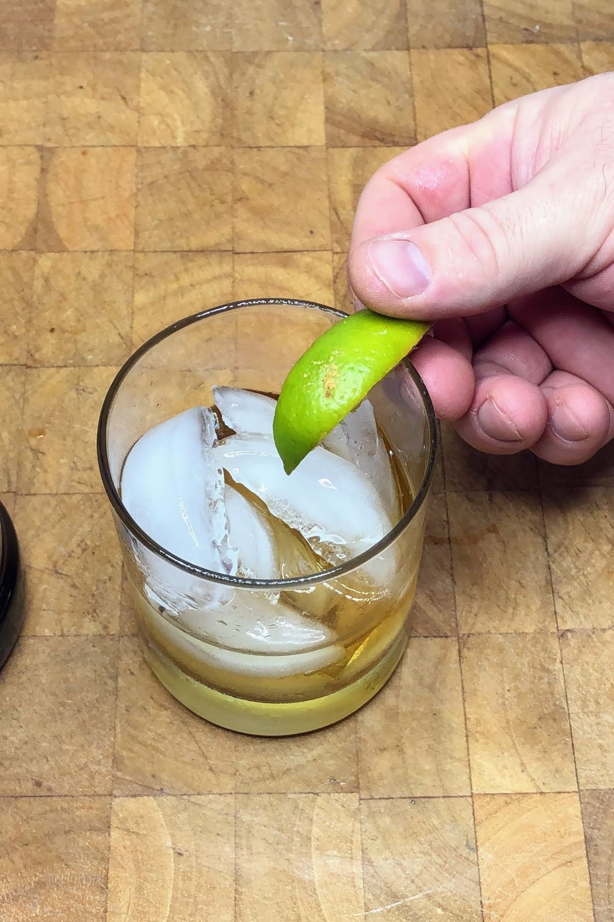 Placing a lime wedge on the glass of a whiskey on the rocks.