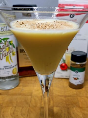 Closeup of eggnog martini with ingredients in background.