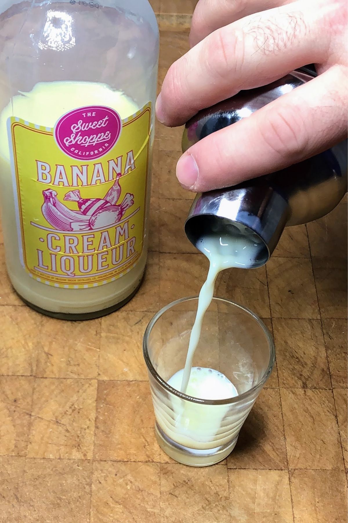 Pouring banana liqueur from shaker into shot glass.