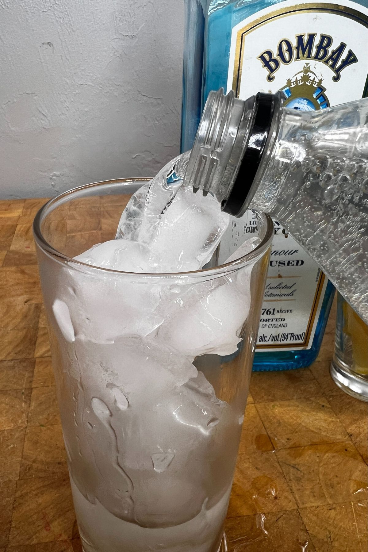 Pouring sprite into a glass with gin.