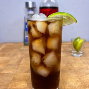 Close up of a tequila and coke in with a lime wedge on the rim.