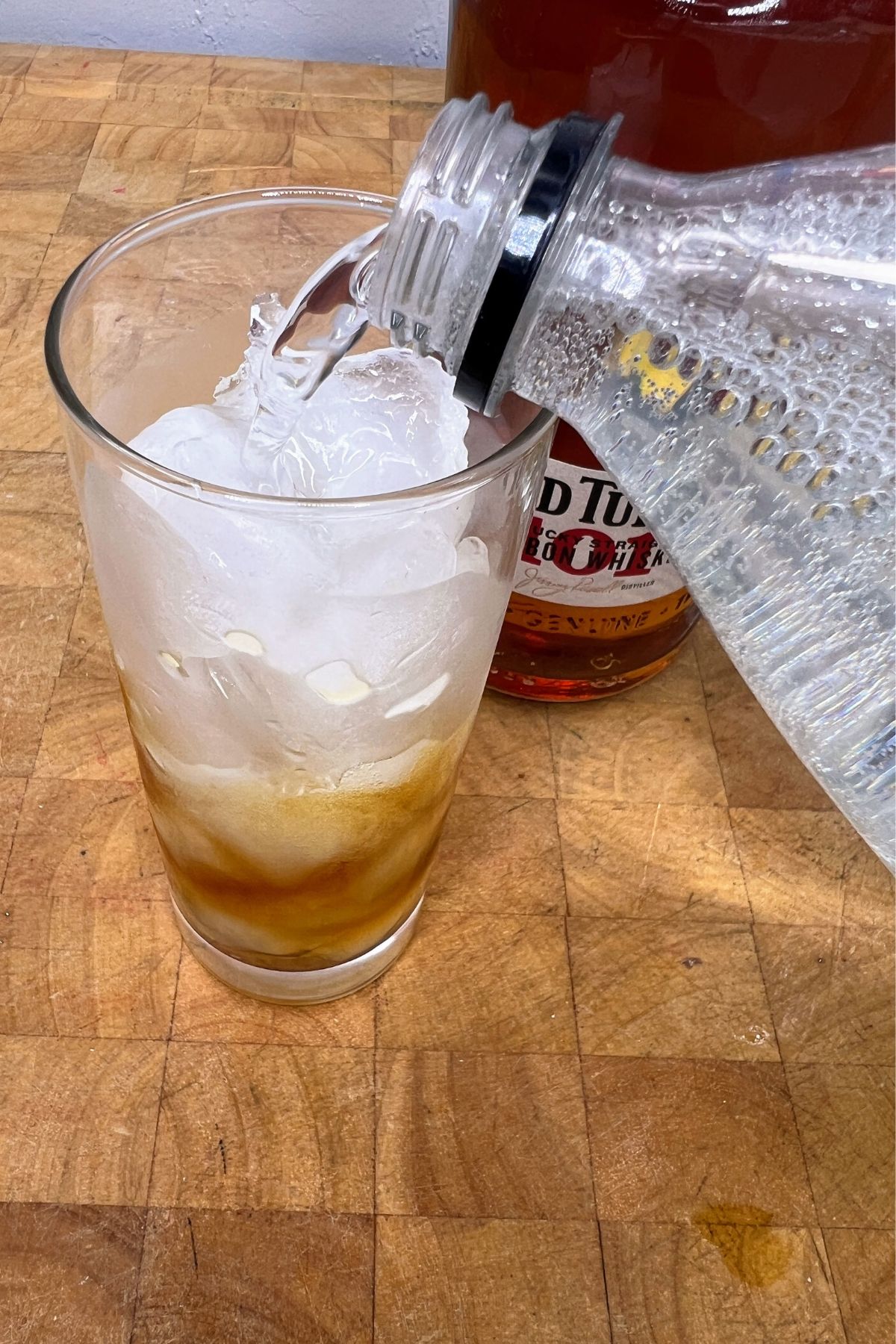 Pouring sprite into a highball glass filled with whiskey.
